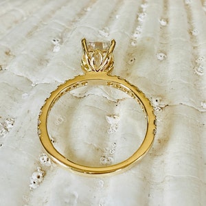 Pode incluir: Um anel de ouro com uma grande gema quadrada transparente engastada em uma delicada configura&ccedil;&atilde;o inspirada em flores. A banda &eacute; adornada com gemas menores.