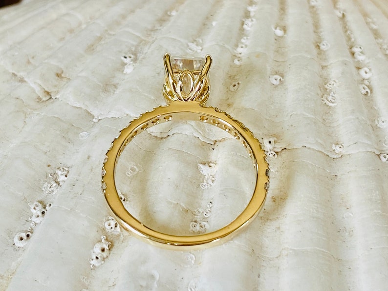Pode incluir: Um anel de ouro com uma grande gema quadrada transparente engastada em uma delicada configura&ccedil;&atilde;o inspirada em flores. A banda &eacute; adornada com gemas menores.
