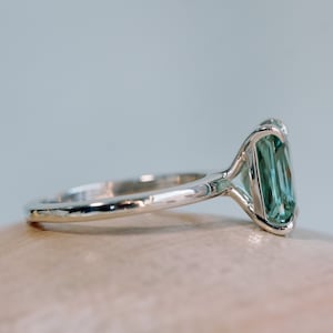 May include: A silver ring featuring a large, emerald-cut green gemstone. The ring has a plain band and a delicate setting for the stone.
