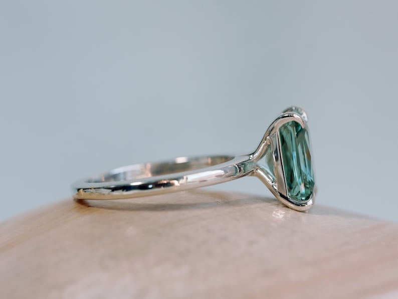 May include: A silver ring featuring a large, emerald-cut green gemstone. The ring has a plain band and a delicate setting for the stone.