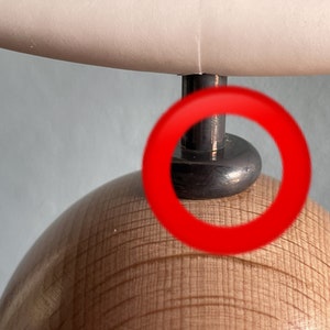 May include: Close-up of a wooden lamp base with a black metal lampshade attachment. The lampshade attachment has a round, shiny, black surface.