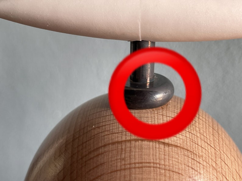 May include: Close-up of a wooden lamp base with a black metal lampshade attachment. The lampshade attachment has a round, shiny, black surface.