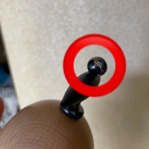 May include: Close-up of a black pepper grinder with a round, silver-colored knob on top. The knob is circled in red.