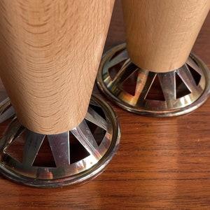 May include: Two wooden table legs with silver metal bases. The bases have a decorative, geometric design.