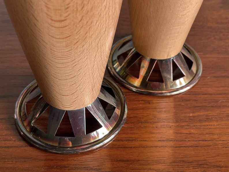 May include: Two wooden table legs with silver metal bases. The bases have a decorative, geometric design.