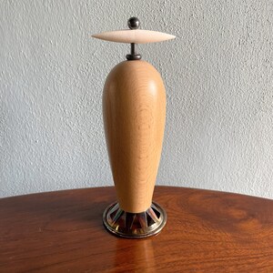 May include: A wooden bottle stopper with a white ceramic top and a metal base. The stopper is shaped like a vase and has a smooth, polished finish.