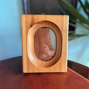 May include: A wooden picture frame with an oval opening. The frame is made of light brown wood and has a natural finish.
