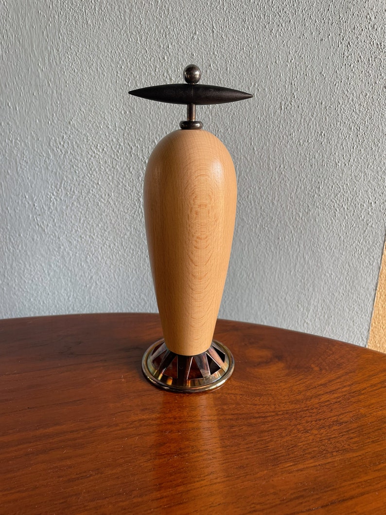 May include: A wooden pepper mill with a black knob on top and a gold metal base.