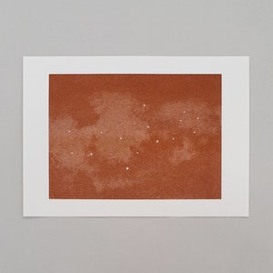 Peut inclure: Une impression abstraite de couleur brun et orange avec des points blancs dispersés sur la surface. L'impression a un aspect texturé, semblable à une aquarelle.