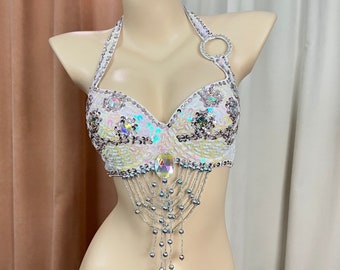 Peut inclure: Haut blanc à bretelles avec des paillettes irisées et des franges de perles. Le haut a un détail de bague sur la bretelle.