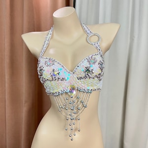 May include: White halter top with iridescent sequins and bead fringe. The top has a ring detail on the halter strap.