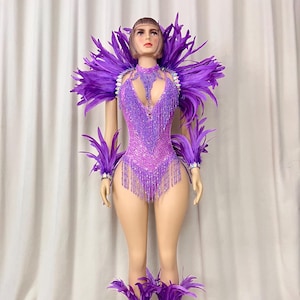 May include: Purple beaded and feathered costume with a halter top, arm cuffs, and leg cuffs. The costume is designed for dancing and performance.