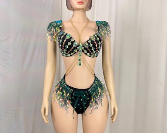May include: A black and green two-piece outfit with fringe and rhinestones. The top is a bra with a gold chain and the bottom is a skirt with a green ribbon.