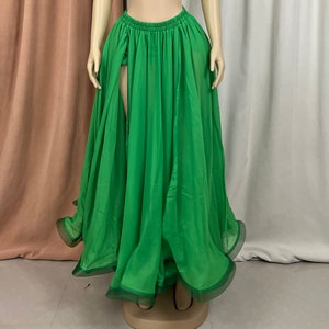 May include: A long, flowing green skirt with a high slit in the front. The skirt is made of a sheer fabric and has a ruffled hem.
