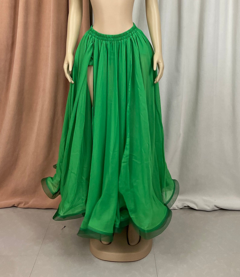 May include: A long, flowing green skirt with a high slit in the front. The skirt is made of a sheer fabric and has a ruffled hem.