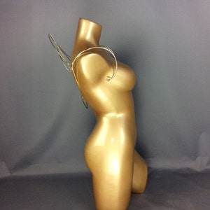 Puede incluir: Una cadena de cuerpo de metal dorado con un diseño de alas. La cadena se lleva en un maniquí dorado.
