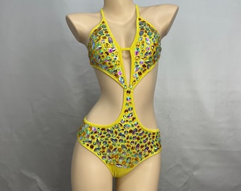 May include: Yellow swimsuit with a halter neckline and cutouts. The swimsuit is covered in iridescent rhinestones.