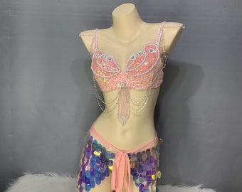 Peut inclure: Un soutien-gorge pailleté rose avec une jupe pailletée assortie bleu et violet irisé. Le soutien-gorge a une frange perlée et la jupe a un lien rose.