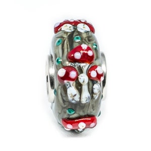 May include: A glass bead with a forest scene featuring red and white mushrooms. The bead is green, brown, and white with a silver metal core.