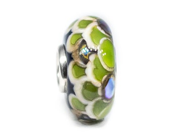 Puede incluir: Una cuenta de vidrio con un diseño floral. La cuenta presenta un patrón de formas verdes y blancas en forma de pétalos sobre un fondo oscuro. Un lazo de metal plateado está unido a la cuenta. La cuenta tiene un acabado brillante y un pequeño acento iridiscente.