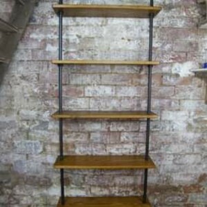 May include: A black metal pipe shelving unit with five wooden shelves. The shelves are mounted to a brick wall.
