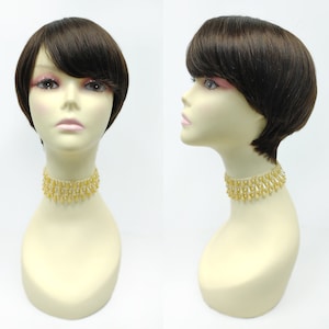 May include: A short brown wig with bangs on a mannequin head. The mannequin is wearing a gold beaded choker necklace.