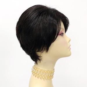 May include: A short black wig with a side part, styled with a choppy, layered look. The wig is displayed on a mannequin head with a gold beaded necklace.