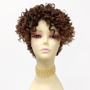 May include: A short, curly brown wig with a side parting. The wig is styled in a pixie cut with tight curls.