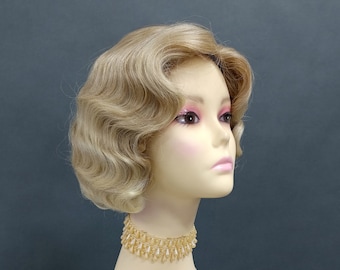 Könnte beinhalten: Eine blonde Perücke mit kurzen, gewellten Locken. Die Perücke ist im Stil eines Vintage-Bob-Haarschnitts aus den 1920er Jahren gestylt. Die Perücke befindet sich auf einem Mannequin-Kopf vor einem hellgrauen Hintergrund.