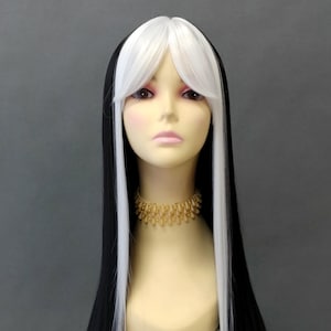Peut inclure: Perruque longue noire et blanche avec une raie au milieu et une frange, présentée sur une tête de mannequin. La perruque présente un contraste saisissant avec des côtés noirs et une section centrale blanche. Un collier doré orne le cou du mannequin.