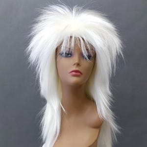 Puede incluir: Una peluca blanca y puntiaguda con mechones largos y en capas y un flequillo corto y deshilachado. La peluca se exhibe en una cabeza de maniquí con un tono de piel neutro, sobre un fondo gris. La textura de la peluca parece voluminosa y texturizada.