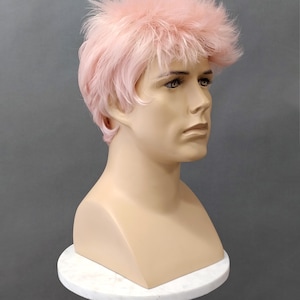 May include: A mannequin head with a light pink wig. The wig has a short, layered style with a textured, feathery top. The mannequin is on a white, round pedestal against a gray background.