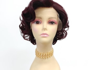 Könnte beinhalten: Eine kurze, burgunderfarbene Perücke mit Seitenscheitel und lockeren Locken. Die Perücke ist im Vintage-Pin-up-Stil gestylt.