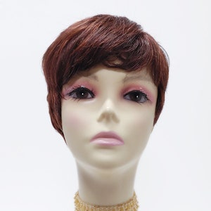May include: A mannequin head with short, choppy, auburn brown hair. The mannequin is wearing a gold beaded choker necklace.