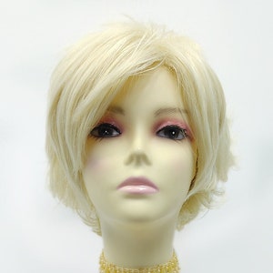 May include: A mannequin head with a short, blonde wig and a beaded choker necklace. The wig has a layered style. The choker is a light yellow color with teardrop-shaped beads. The mannequin has a neutral skin tone and is set against a white background.