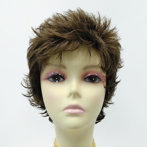 Puede incluir: Una peluca corta marrón con capas irregulares en una cabeza de maniquí. El maniquí lleva un collar de gargantilla de cuentas doradas.