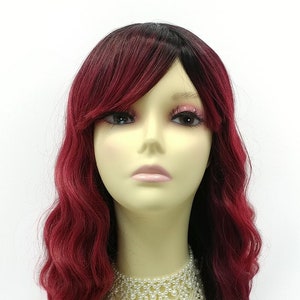 May include: A long, wavy wig with dark red and black hair. The wig is styled with a side part and a fringe. The wig is worn on a mannequin head with a white pearl necklace.