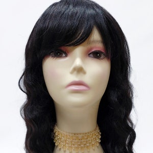 May include: A black wig with long, wavy hair and a side part. The wig is styled with bangs and is worn on a mannequin head. The mannequin is wearing a light brown beaded choker necklace.