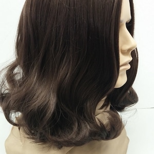 May include: A brown wig with shoulder-length, wavy hair. The wig is styled with a side part and has a natural-looking hairline. The hair is a rich, dark brown color and has a slight sheen. The wig is displayed on a mannequin head.