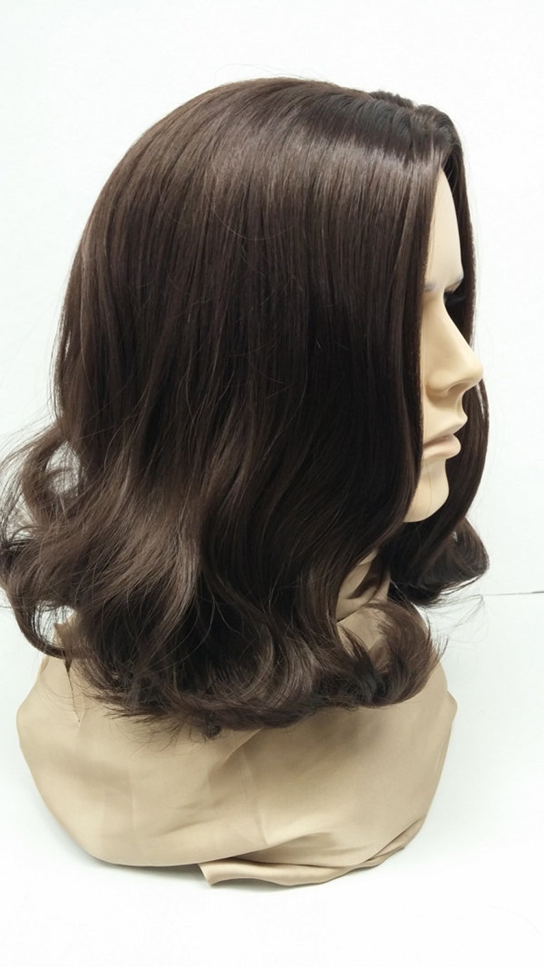 May include: A brown wig with shoulder-length, wavy hair. The wig is styled with a side part and has a natural-looking hairline. The hair is a rich, dark brown color and has a slight sheen. The wig is displayed on a mannequin head.