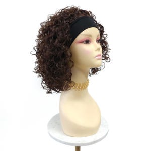 May include: A brown curly wig styled with a solid black headband, displayed on a mannequin head. The hair features tight, voluminous curls in a dark brown shade, and the black headband is positioned across the forehead to secure the hair.