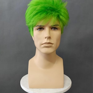 May include: A mannequin head with a vibrant green wig. The wig features short, textured layers, creating a spiky, voluminous style. The mannequin is displayed on a white, round pedestal with a gold-colored stem, against a gray backdrop.