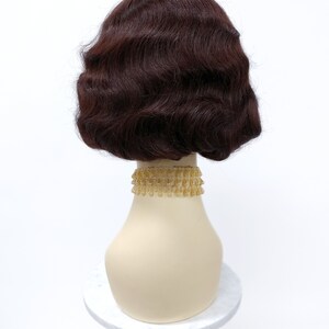 May include: A brown wig with a wavy style, styled in a bob shape. The wig is on a mannequin head with a gold beaded necklace.