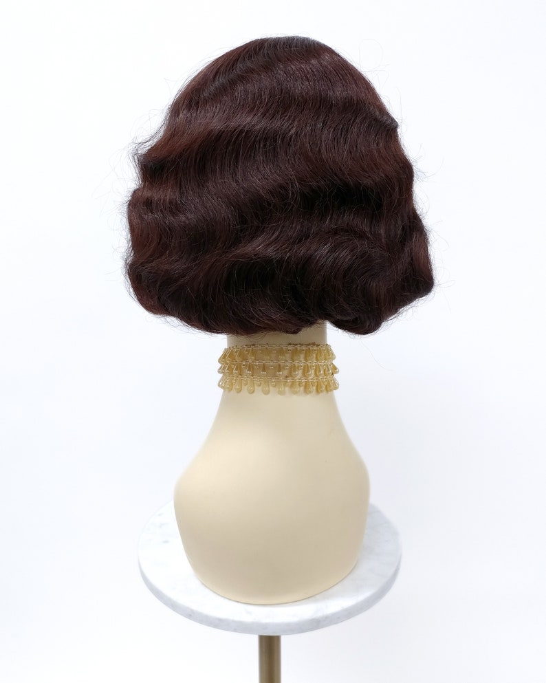 May include: A brown wig with a wavy style, styled in a bob shape. The wig is on a mannequin head with a gold beaded necklace.