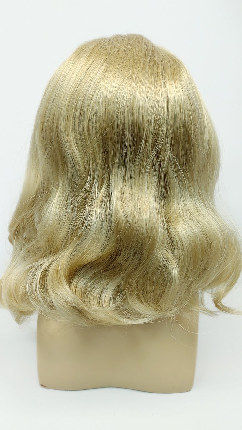 Peut inclure: Une perruque blonde avec un style ondul&eacute;. La perruque est sur une t&ecirc;te de mannequin.