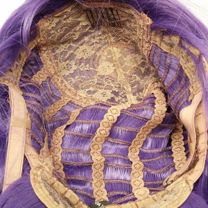 May include: The inside of a purple wig with a lace front and adjustable straps. The wig is made of synthetic hair and has a natural looking hairline.