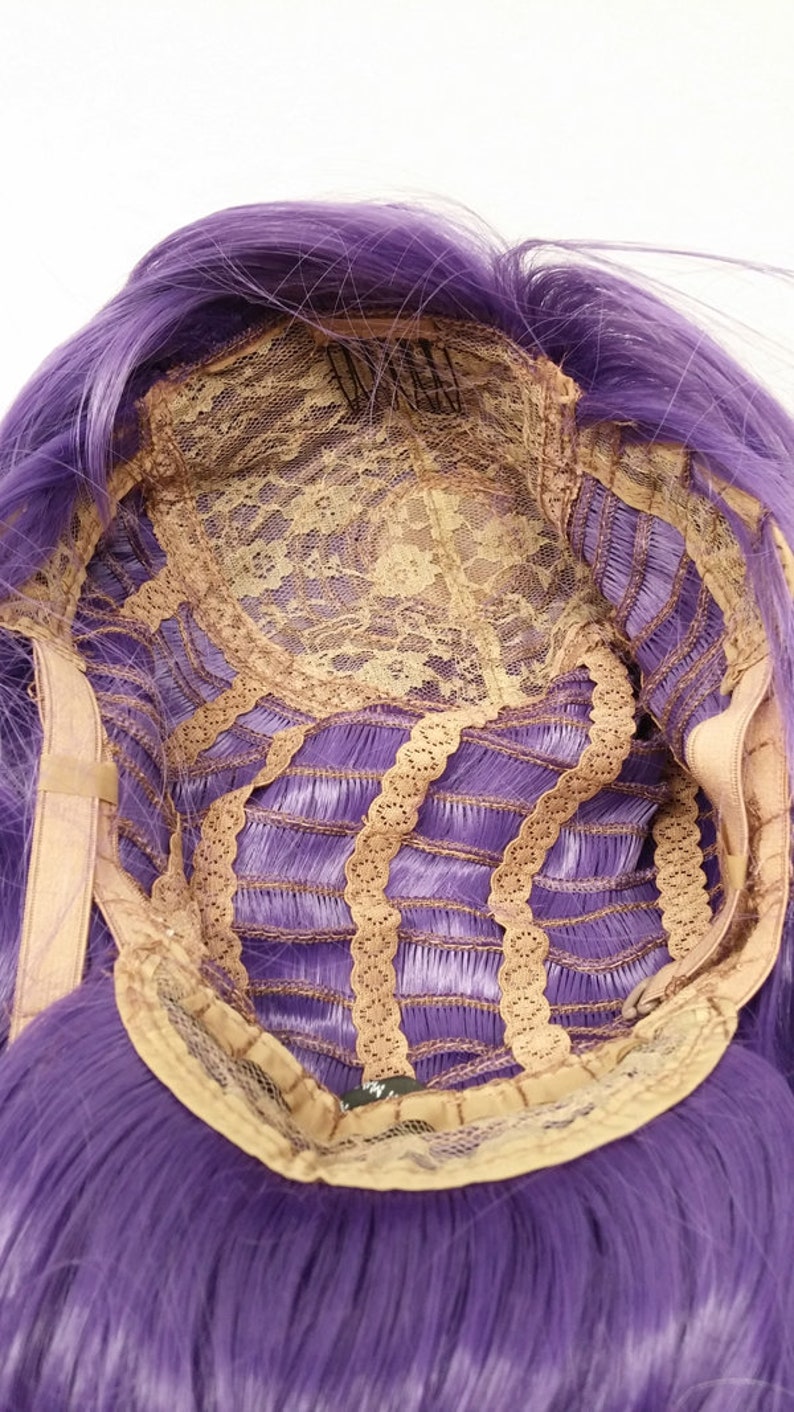 May include: The inside of a purple wig with a lace front and adjustable straps. The wig is made of synthetic hair and has a natural looking hairline.