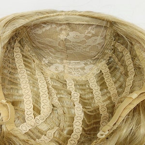 Peut inclure: L'int&eacute;rieur d'une perruque blonde avec une frange en dentelle et des sangles r&eacute;glables. La perruque est de construction tiss&eacute;e et est faite de cheveux synth&eacute;tiques.