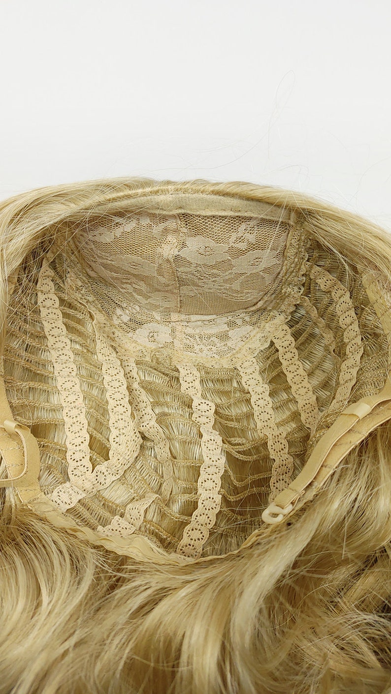 Peut inclure: L'int&eacute;rieur d'une perruque blonde avec une frange en dentelle et des sangles r&eacute;glables. La perruque est de construction tiss&eacute;e et est faite de cheveux synth&eacute;tiques.