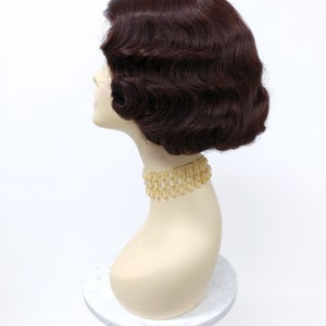 May include: A dark brown wig with a vintage style, featuring soft waves and a short bob cut. The wig is displayed on a mannequin head.